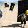 A line of workers carry solar panels at a solar energy site.