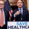 Chuck Schumer stands next to Hakeem Jeffries as he speaks at a podium with the sign "Save Healthcare."