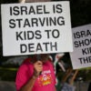 Anti-Israel protesters hold signs reading "Israel is Starving Kids to Death" and "Israel Shoots Kids in the Head" during rally.