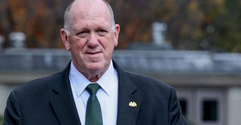 A smiling Tom Homan in a black suit with green tie.
