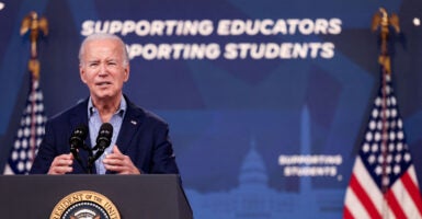 Then-President Joe Biden behind a podium speaks in front of a blue backdrop with white lettering reading 