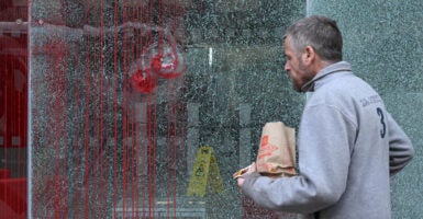 A man in grey jacket walks past a shattered window that's covered in fake blood.