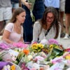 Two women kneel amid a flower memorial.