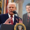 President Trump speaks at a podium, a portrait of Ronald Reagan behind him.