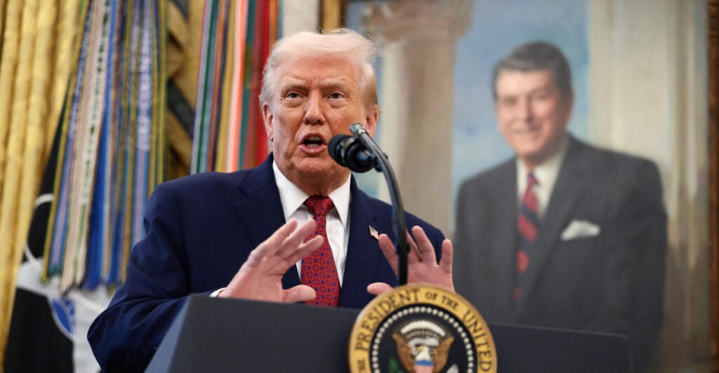 President Trump speaks at a podium, a portrait of Ronald Reagan behind him.