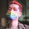 A thin young man with dyed red hair, makeup and a rainbow mask.