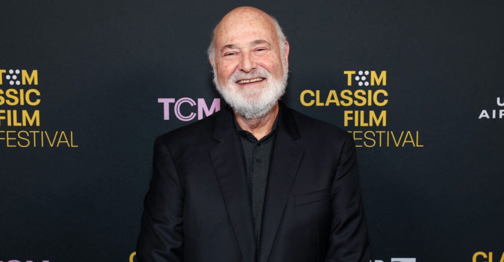 A smiling Rob Reiner in black in front of a TCM Classic Film Festival backdrop