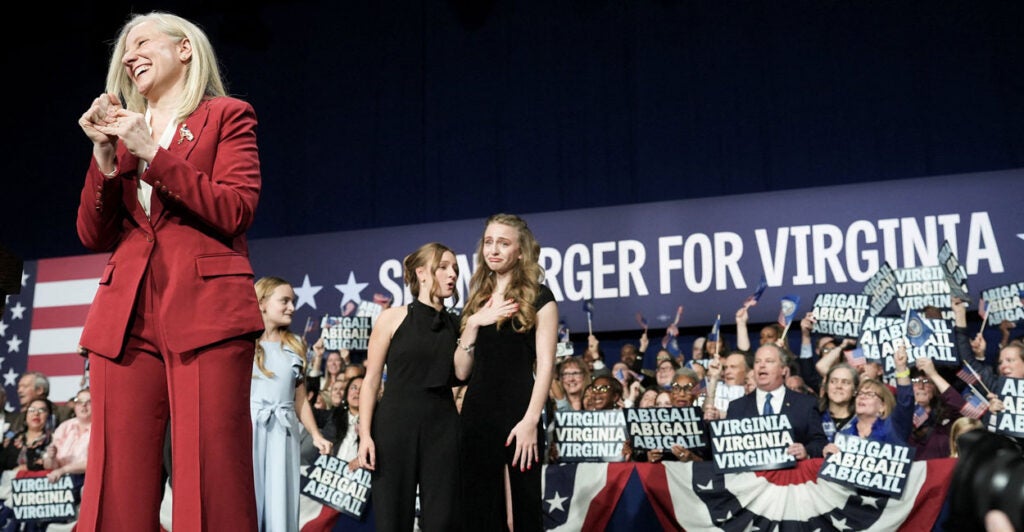 Abigail Spanberger in a red suit smiles at victory rally, while little girl behind her appears to cry with pride.