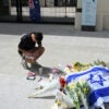 Man kneels while writing at edge of memorial for Bondi Beach Hanukkah massacre victims.