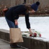 A woman holding shopping bag lays flowers down near site of Brown University shooting.