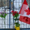 A small Canadian flag and flowers placed against a fence.