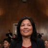Julie Su sits at table for a Senate hearing, with row of people seated behind her.