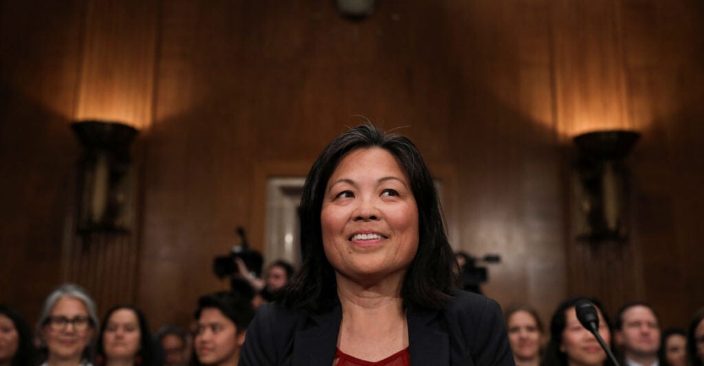 Julie Su sits at table for a Senate hearing, with row of people seated behind her.