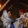 A couple plays Mary and Joseph with the male holding an infant.