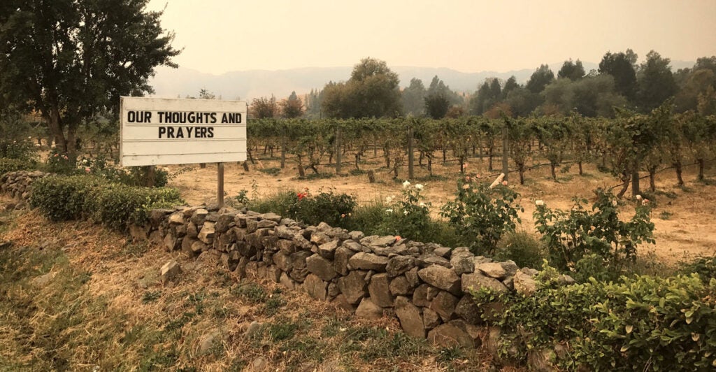Smoky haze covers a winery in Sonoma, CA. A sign reads "Our Thoughts and Prayers."