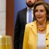 Nancy Pelosi in a yellow jacket and white shirt walks in a hallway of the U.S. Capitol.