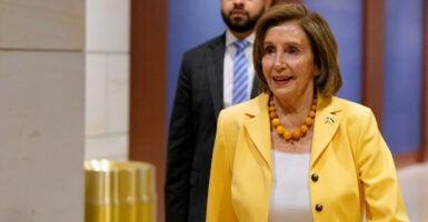 Nancy Pelosi in a yellow jacket and white shirt walks in a hallway of the U.S. Capitol.
