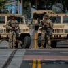 Two National Guardsmen stand in front of Jeeps on street in Santa Ana, California.