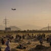 A military transport flies over an Afghan field, as Afghans watch below.