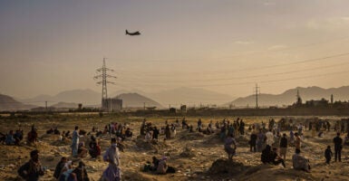 A military transport flies over an Afghan field, as Afghans watch below.