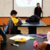 Children and adults sit at a table with coloring supplies at a child care facility.