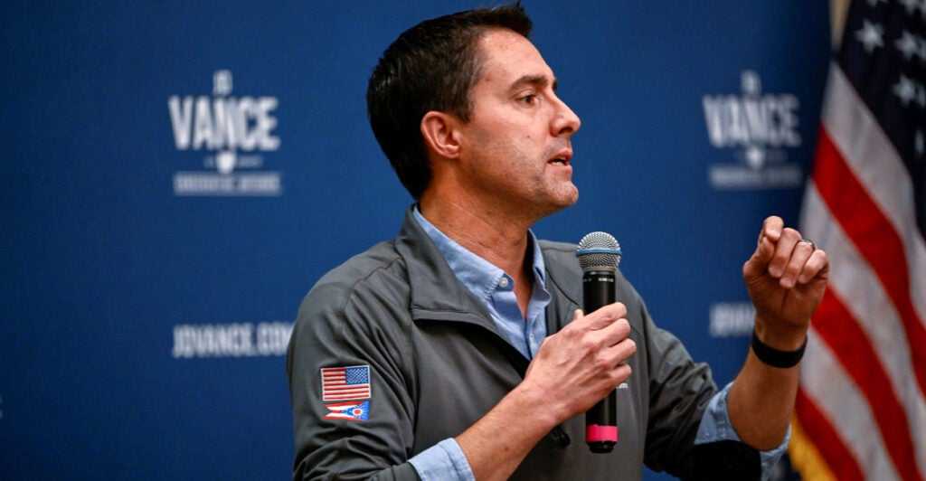 Secretary of State Frank LaRose speaks to a crowd as he holds a microphone.