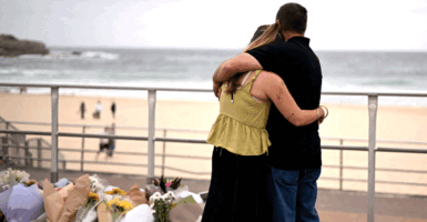 TOPSHOT - Mourners embrace near tributes piled together in memory of the victims of a shooting at Bondi Beach, in Sydney on December 16, 2025. Australia's leaders have agreed to toughen gun laws after attackers killed 15 people at a Jewish festival on Bondi Beach, the worst mass shooting in decades decried as antisemitic "terrorism" by authorities. (Photo by Saeed KHAN / AFP via Getty Images)