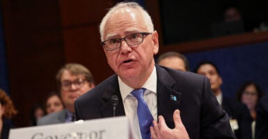 Minnesota Gov. Tim Walz gestures at himself in a suit. Minnesota bureaucrats have accused Walz of enabling fraud on a massive scale.