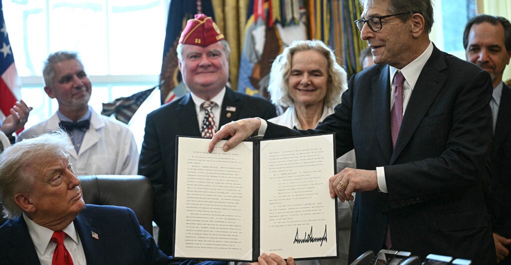 President Trump looks up from his desk at signed executive order being held by an aide, as other slook on.