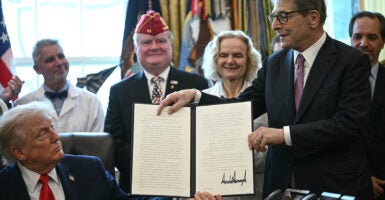 President Trump looks up from his desk at signed executive order being held by an aide, as other slook on.