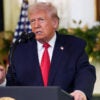 President Trump speaks at a podium in the White House with a backdrop of Christmas garland.
