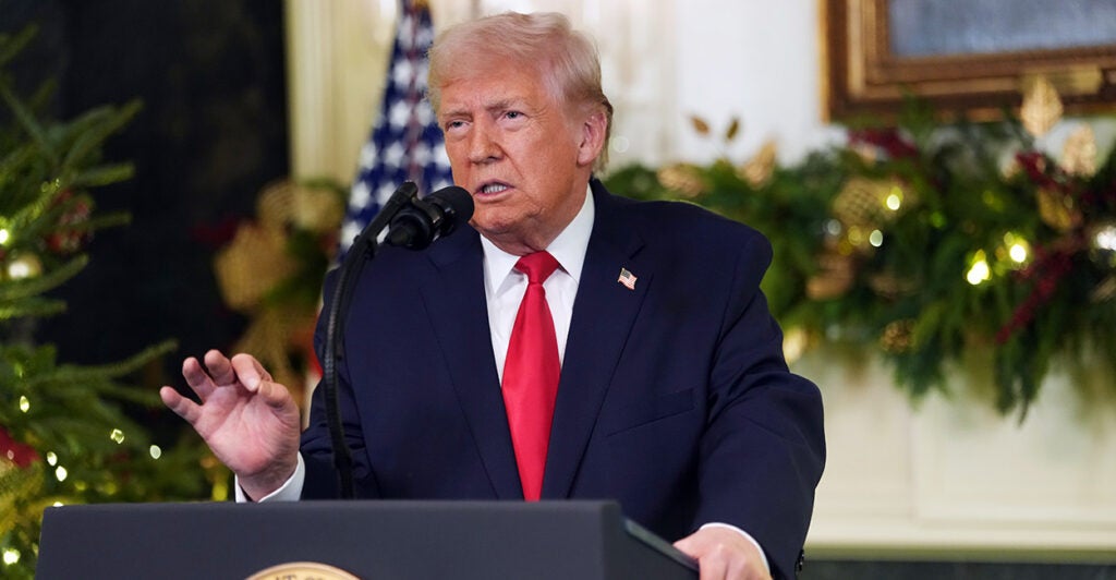 President Trump speaks at a podium in the White House with a backdrop of Christmas garland.