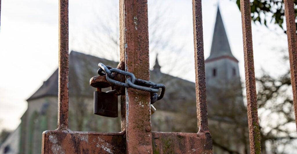 A chain lock on a rusted iron gate, with church in the background.