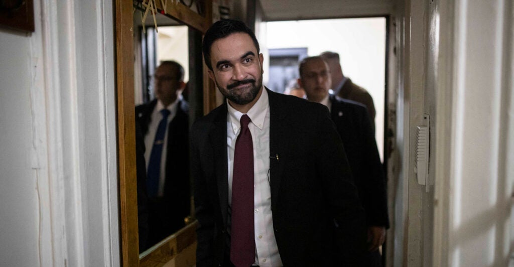 Zohran Mamdani walks in an apartment building hallway.