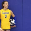 Transgender volleyball player Blaire Fleming, in a yellow San Jose State uniform, holds a volleyball, preparing to serve.