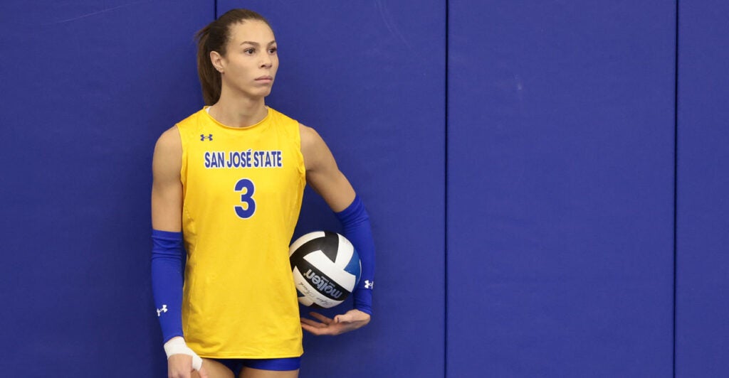 Transgender volleyball player Blaire Fleming, in a yellow San Jose State uniform, holds a volleyball, preparing to serve.