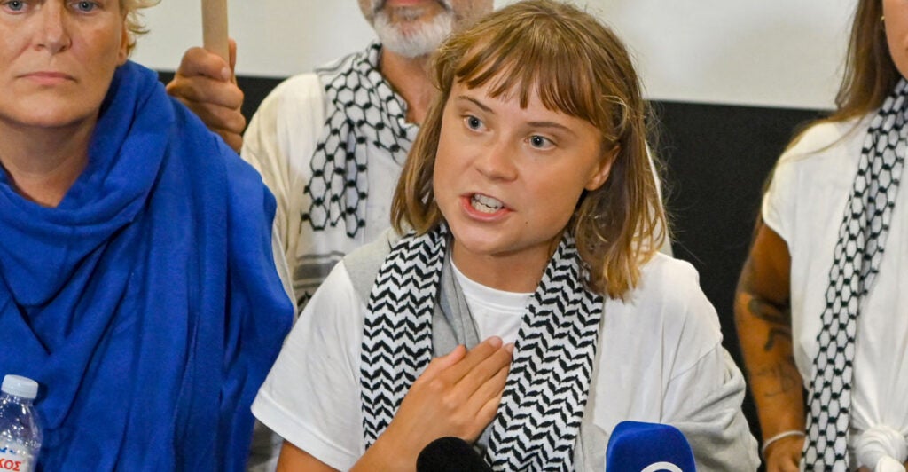 Greta Thunberg, with her hand at her chest, speaks at a press conference.