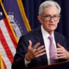 Federal Reserve Chairman Jerome Powell gestures while speaking at a podium in front of American flags.