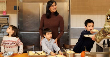 Usha Vance in a brown shirt stands in front of her three young children as they serve meals to soldiers.