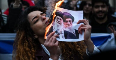An anti-Iranian regime protester lights a cigarette with a lit paper depicting Ali Khamenei, Supreme Leader of Iran during a gathering.