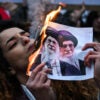 An anti-Iranian regime protester lights a cigarette with a lit paper depicting Ali Khamenei, Supreme Leader of Iran during a gathering.