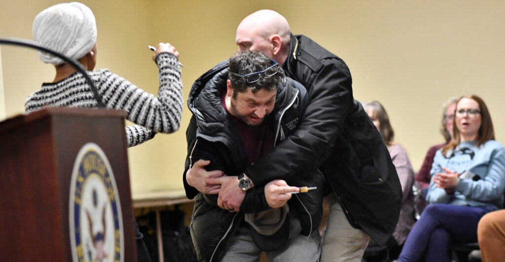 A man is tackled after spraying an unknown substance at US Representative Ilhan Omar (D-MN) (L) during a town hall she was hosting in Minneapolis, Minnesota, on January 27, 2026. US Democratic congresswoman Ilhan Omar was targeted during a speech late on January 27 by a man who sprayed an unidentified liquid at her from a syringe before being tackled by security guards, according to an AFP journalist at the scene. The man was led out of the premises as Omar, a frequent target of attacks by President Donald Trump, continued her speech saying "we will stay resilient in the face of whatever they might throw on us." (Photo by Octavio JONES / AFP via Getty Images)