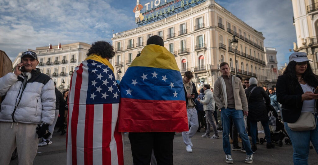 MADRID, SPAIN - 2026/01/03: A couple wearing the flag of Venezuela and the flag of the United States of America. Thousands of Venezuelans living in Madrid gathered at Puerta del Sol to celebrate the arrest of President of Venezuela Nicolas Maduro after President of the United States of America Donald Trump announced that US forces had captured Venezuela's leader after bombing Caracas. (Photo by Marcos del Mazo/LightRocket via Getty Images)