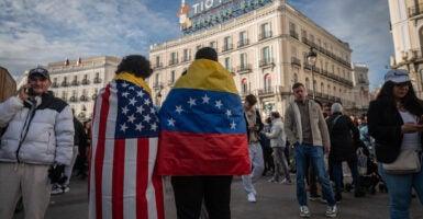 MADRID, SPAIN - 2026/01/03: A couple wearing the flag of Venezuela and the flag of the United States of America. Thousands of Venezuelans living in Madrid gathered at Puerta del Sol to celebrate the arrest of President of Venezuela Nicolas Maduro after President of the United States of America Donald Trump announced that US forces had captured Venezuela's leader after bombing Caracas. (Photo by Marcos del Mazo/LightRocket via Getty Images)