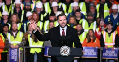 Vice President JD Vance stands at a lectern while factory members stand behind him.