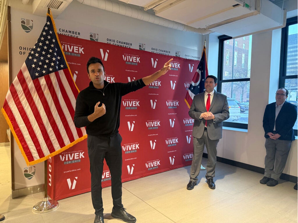 Vivek Ramaswamy gestures to the crowd with a campaign banner behind him.
