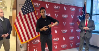 Vivek Ramaswamy gestures as he stands in front of a campaign backdrop.