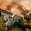Firefighters coordinate their efforts, aiming hoses at a house with flames consuming its roof in Pacific Palisades, California, on January 8, 2025.