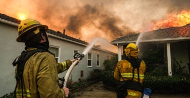 Firefighters coordinate their efforts, aiming hoses at a house with flames consuming its roof in Pacific Palisades, California, on January 8, 2025.