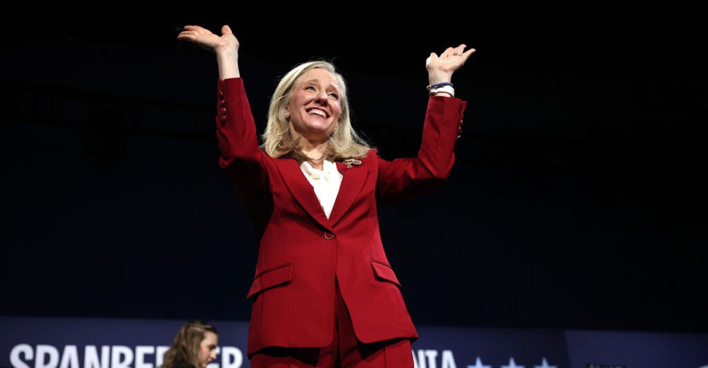 Abigail Spanberger in a red suit with her arms raised.